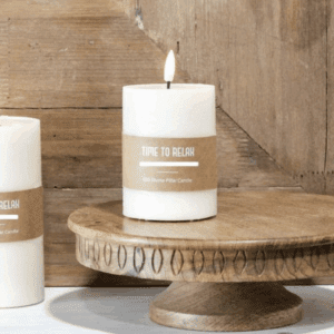 White candle burning on a rustic wooden cake stand.